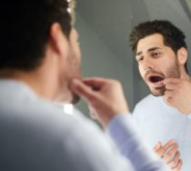 Man with broken tooth looking at his smile in the mirror