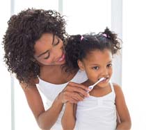 Mother helping her child brush her teeth