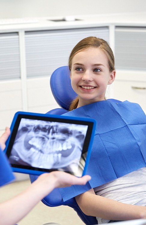 Dentist looking at young girl's digital dental x-rays on tablet computer