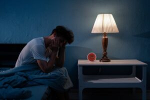 Man sitting on edge of bed during middle of the night.