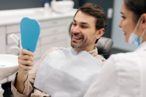 Dental patient admiring results in handheld mirror.